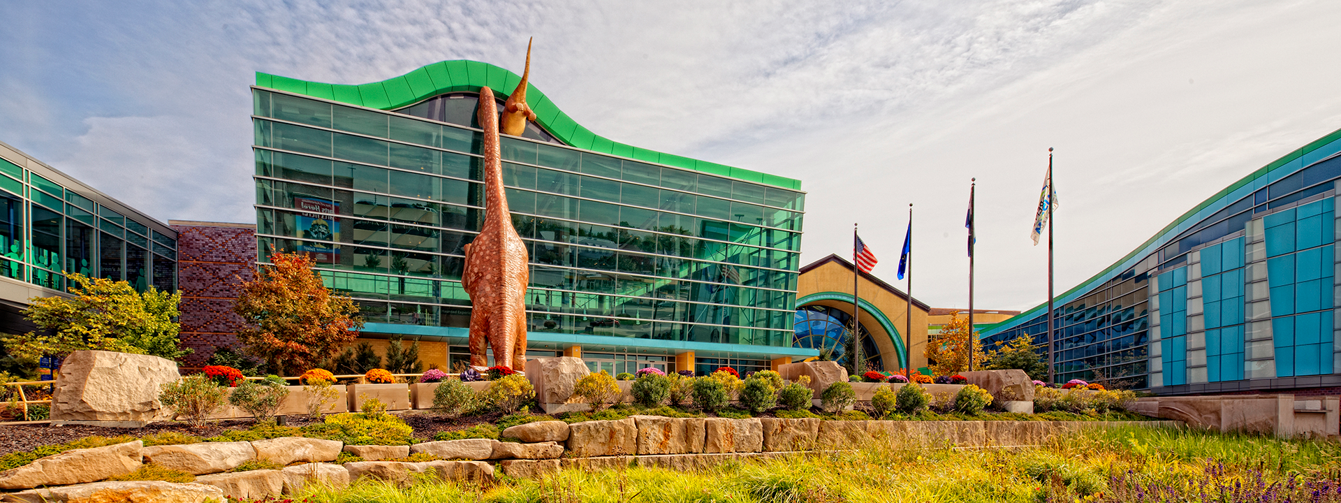 Exterior of The Children's Museum showing a dinosaur peeking into the building.