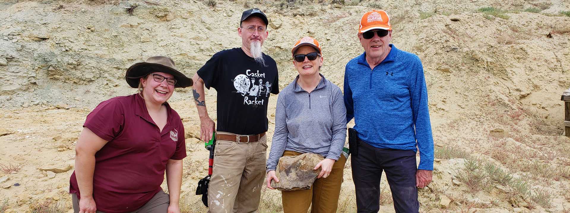 Steven and Susan Haines posing with two scientists at the Jurassic Mile dig site in Wyoming. Susan is holding a fossil.