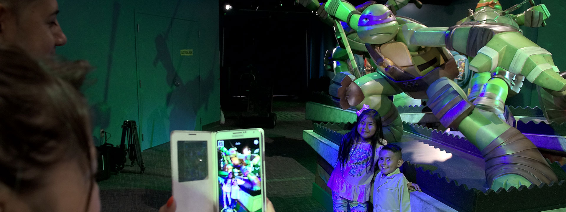 Children getting their photo taken in front of life-sized sculptures of the Teenage Mutant Ninja Turtles.