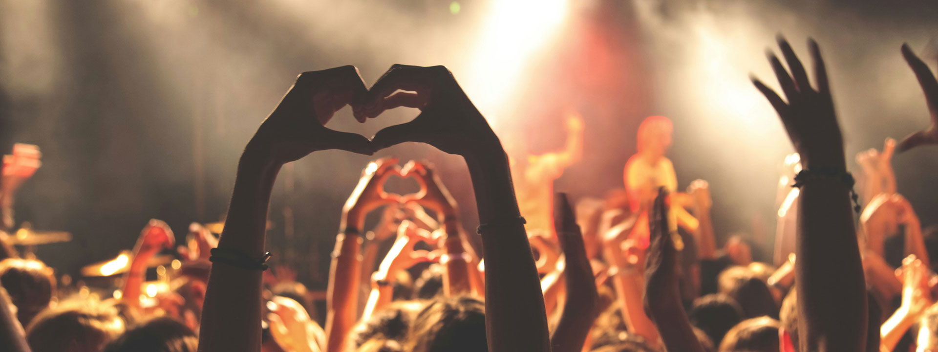 Crowd at a concert with people forming hearts with their hands.