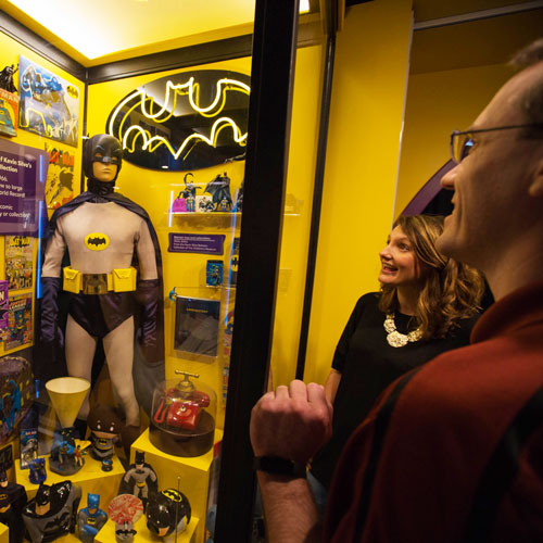 Grown-ups looking at a Batman display inside the American POP exhibit.