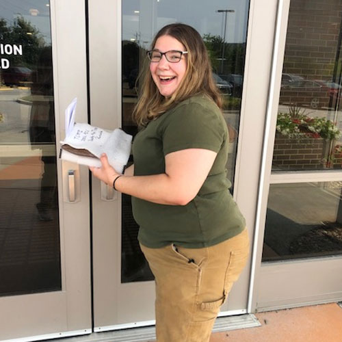 Paleontology Curator Laura Rooney standing outside Eli Lilly and Company while holding Bucky's furcula wrapped in protective cloth.