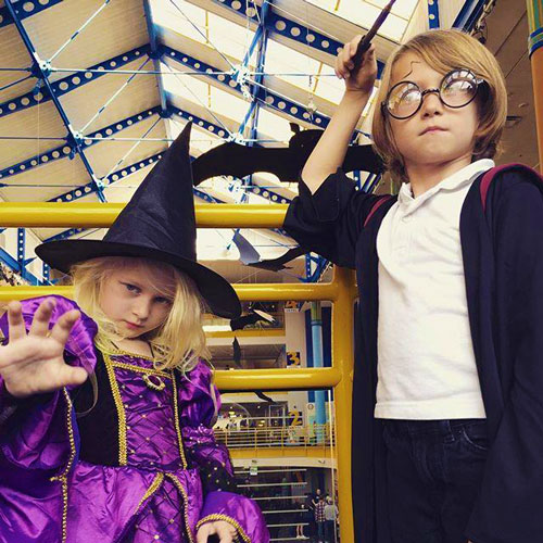 Child on the left is wearing a purple witch's costume and the child on the right is wearing a Harry Potter robe and glasses, holding up a wand