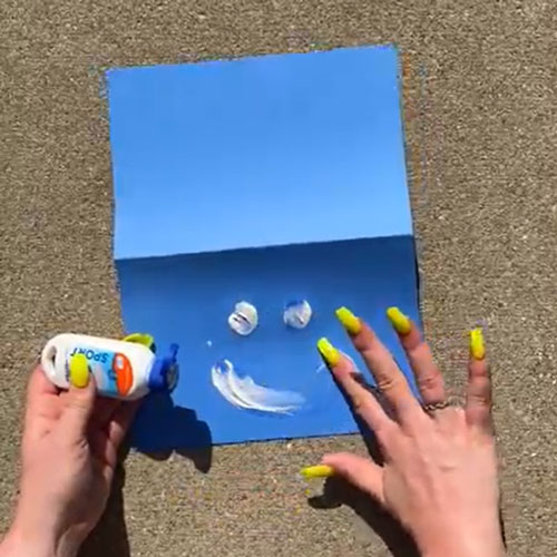 Hands with lime green fingernails making a smiley face out of sunblock on a blue square piece of paper.