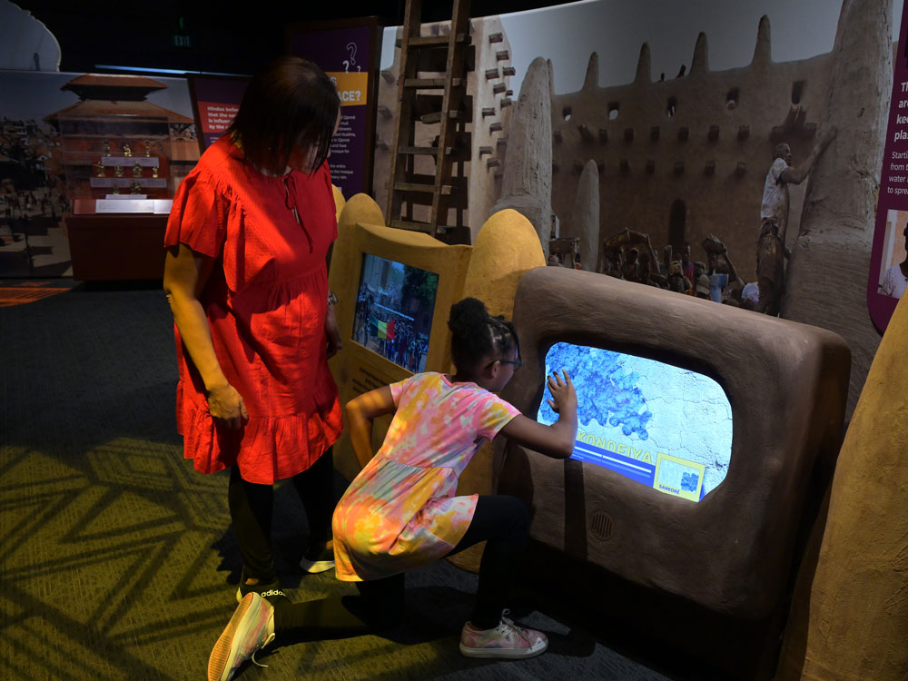 Child playing with the interactive computer screen to replaster the virtual mosque.