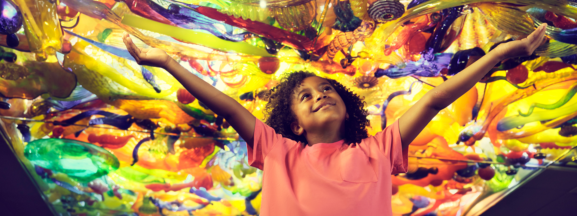 Child with outstretched arms under the Fireworks of Glass ceiling.