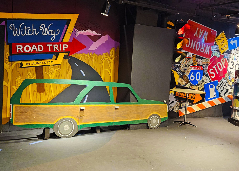 Large cutout photo op of a station wagon with the Witch Way Road Trip logo behind it.